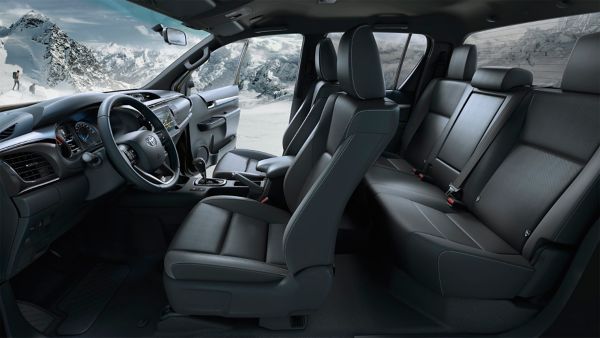 Innenraum des Toyota Hilux mit dunklen Sitzen, im Hintergrund ist durch die offene Beifahrertür eine schneebedeckte Berglandschaft zu sehen.